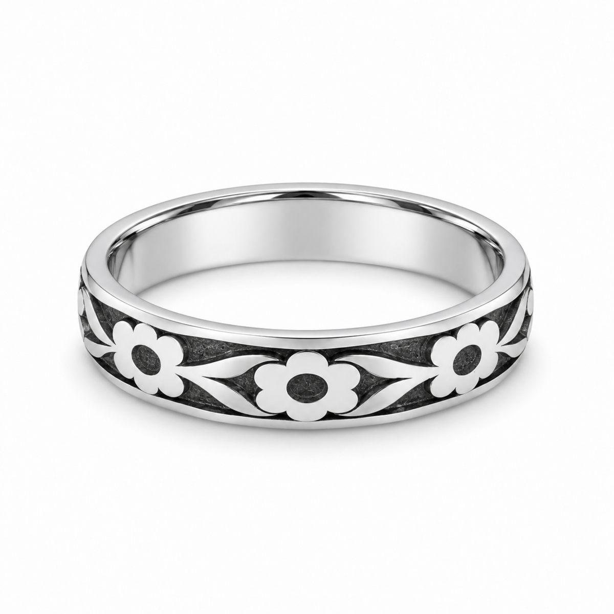 A platinum wedding ring featuring a raised floral pattern with white flower petals and dark oxidized centers and background details.