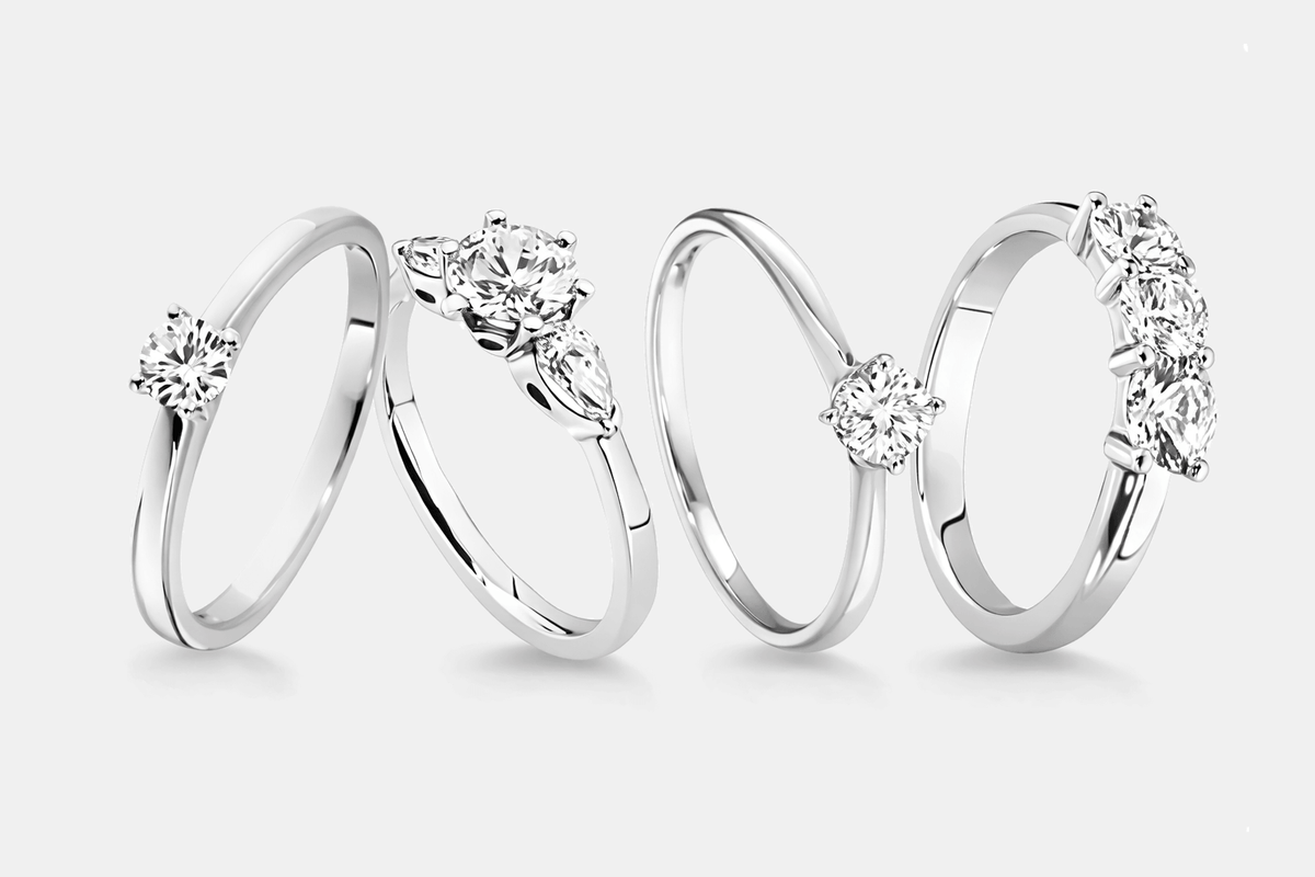 Four platinum engagement rings with diamond accents on a white background