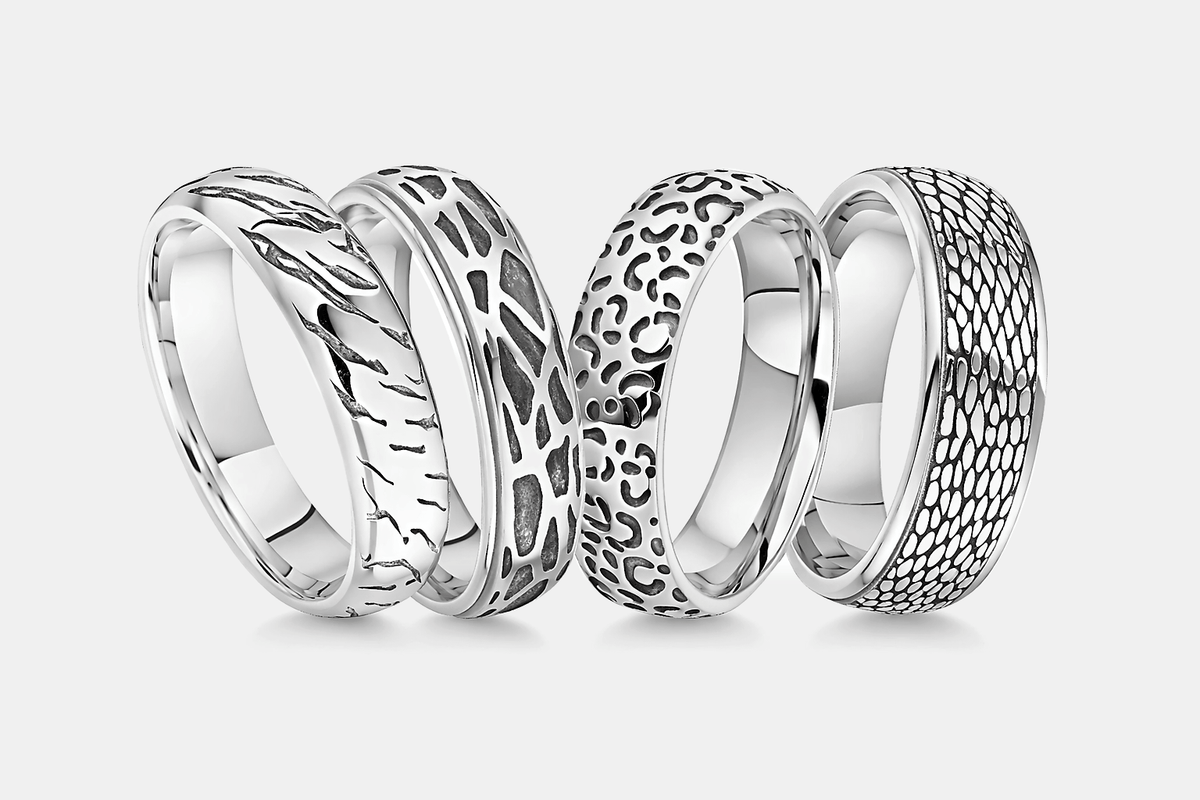 Four platinum wedding rings with animal textured designs on a white backgrounds