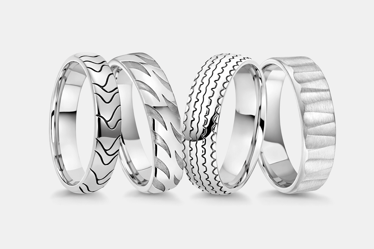 Four platinum wedding rings with unique patterns on a light gray background